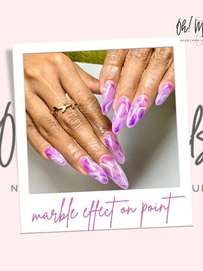 A lovely lilac marble effect. This design uses shades of purple and white to create a soft, swirling marble pattern on long, stiletto-shaped nails.