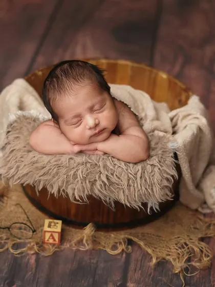 A wider view of the newborn in the bucket, with a few props like a letter block and tiny glasses to hint at a 'little scholar' theme.