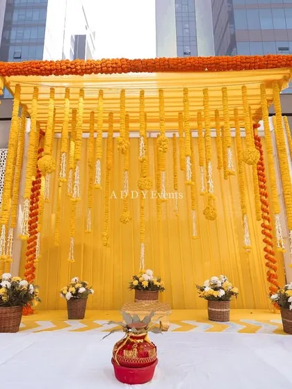 A traditional Haldi mandap setup, featuring a canopy of yellow drapes and decorated with strings of fresh marigolds.