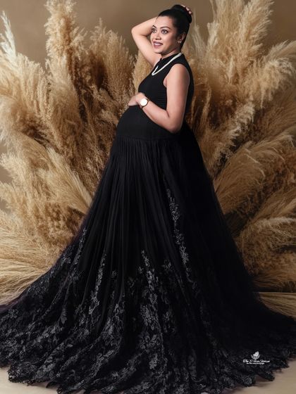 A dramatic solo portrait featuring a stunning black gown with an intricate lace train. The backdrop of pampas grass adds texture and a touch of boho flair.