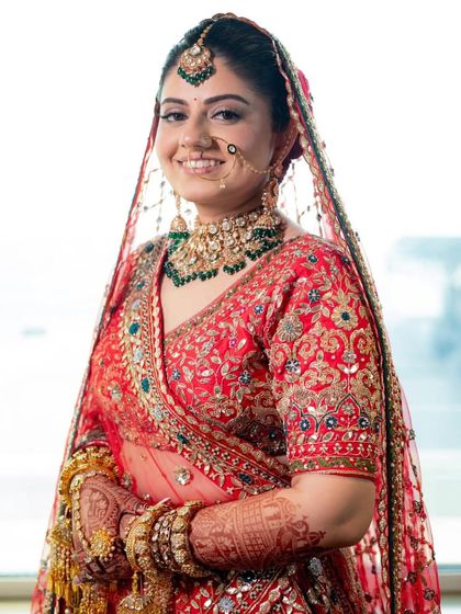 A beautiful portrait of a bride in her red wedding lehenga, showcasing the intricate embroidery and matching jewellery.