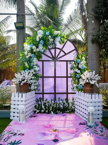 A full view of the charming photo corner. The window backdrop, picket fences, and floral carpet create a whimsical and picturesque spot for the couple and their guests.