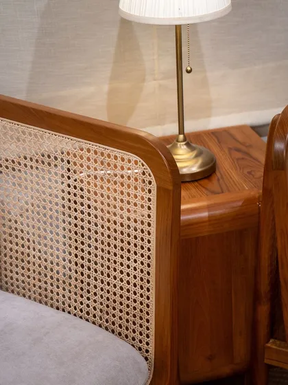 A detail shot showing the interplay of textures between a rattan armchair and a solid teak 'Cuo' side table.