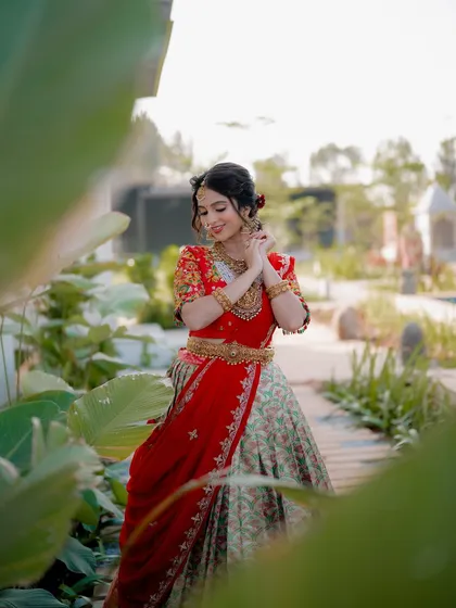 A candid shot of a model in a traditional half saree, framed by lush greenery. The composition creates a sense of depth and makes the outfit stand out.