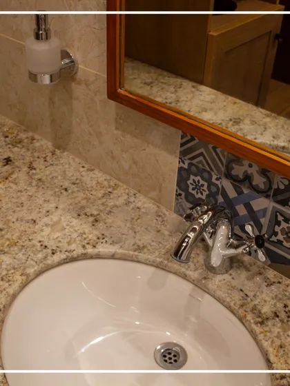 Detail is everything in historic preservation. This close-up of the gents' washroom sink shows the interplay of textures, from the speckled colonial gold stone to the smooth ceramic basin and the classic design of the chrome faucet, all set against a backdrop of decorative tiles.
