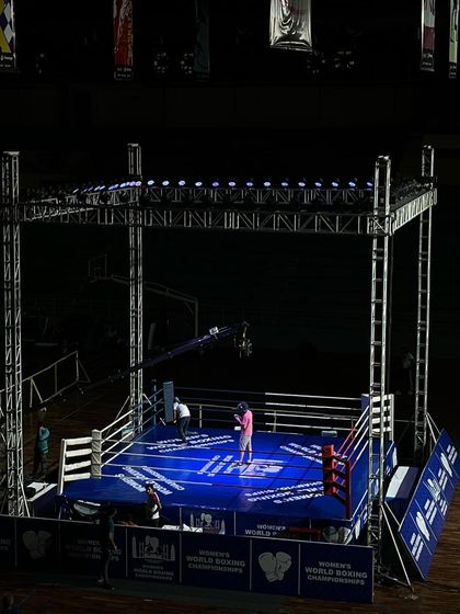 A lone figure stands in the professionally lit boxing ring before an event. This atmospheric shot highlights the calm before the storm at the Women's World Boxing Championships.