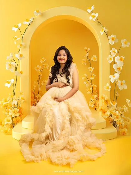 A sweet and joyful portrait. The mother-to-be is seated within a floral yellow arch, her smile radiating the happiness and excitement of this special time.