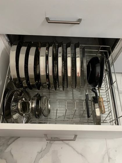 A wire basket drawer organized with a rack for plates and lids. This is a great solution for heavy steel items, providing sturdy and accessible storage.