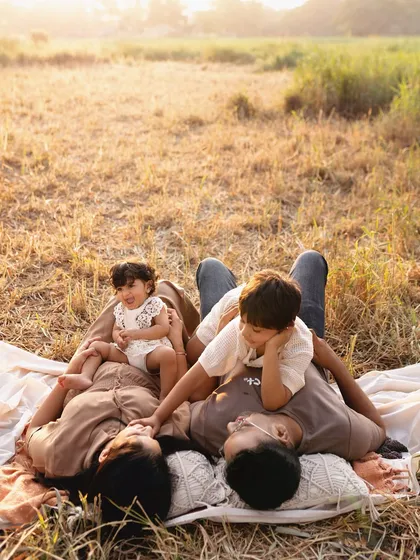 A quiet moment during a family picnic. The whole family lies together on a blanket, enjoying the golden hour light and each other's company.