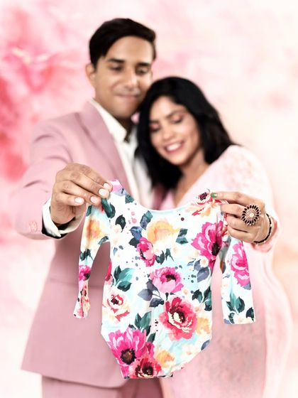 A beautiful couple shares their excitement by holding up a floral onesie. The coordinated pink outfits and backdrop make this a perfectly styled pregnancy announcement.
