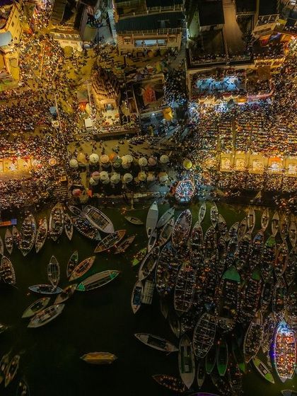 A night aerial shot of the ghats during Dev Deepawali in Varanasi. The frame is filled with the chaos and beauty of countless boats and people celebrating under the bright lights.