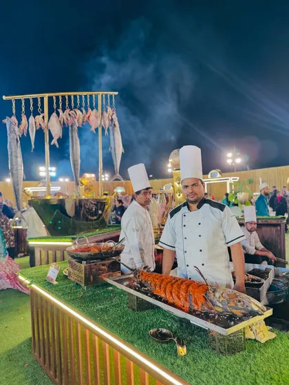 A chef proudly presents a large, perfectly grilled lobster at our live seafood counter. This premium offering highlights my commitment to sourcing and preparing the finest ingredients for your event.