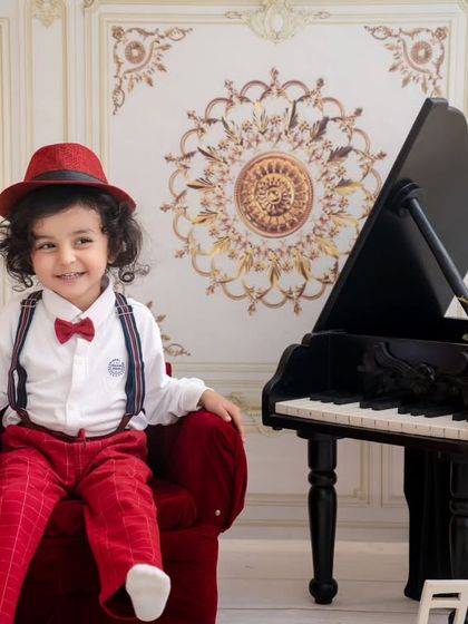 This little maestro is ready for his performance, sitting confidently in his red chair next to the piano.