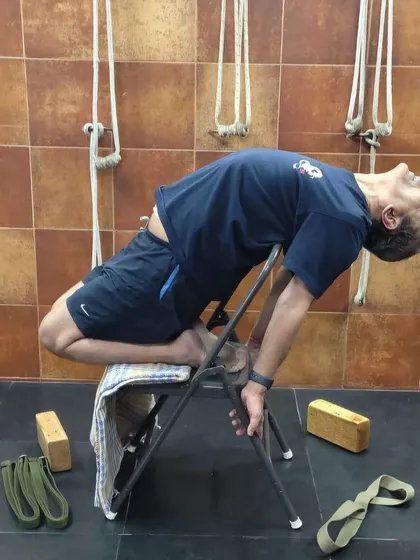 A demonstration of Laghu Vajrasana (Little Thunderbolt Pose) over a chair. This prop makes this deep backbend more accessible and helps to open the quadriceps and chest.
