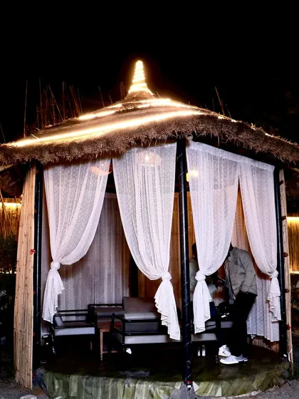 Your own private corner under the stars. This is one of our bamboo cabanas at night, perfect for intimate conversations or a quiet dinner. The sheer curtains and warm lighting create a cozy, secluded feel.
