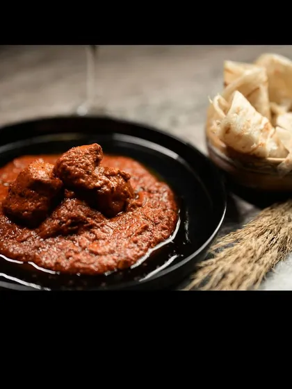 A serving of my Angara Murg Korma, a smoky and spicy chicken curry, plated in a dark bowl with rumali roti on the side. The moody lighting enhances the dish's rich, deep colors.