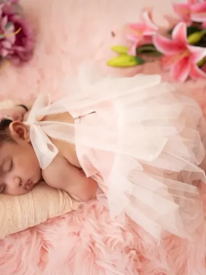 A side view of a newborn sleeping on her tummy, showing the lovely details of her pink dress and the soft floral arrangement. We capture various poses for a complete gallery.