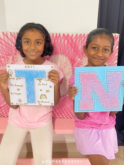 Two young sisters show off their personalized initial string art projects, a fun and creative activity they did together.