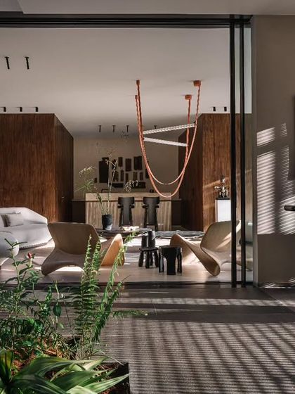 The main living room, featuring a mix of modern furniture and a statement orange light fixture. The space opens up completely to the outdoors, creating a seamless flow between the living area and the garden.