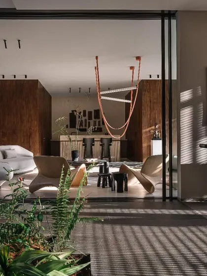 The main living room, featuring a mix of modern furniture and a statement orange light fixture. The space opens up completely to the outdoors, creating a seamless flow between the living area and the garden.