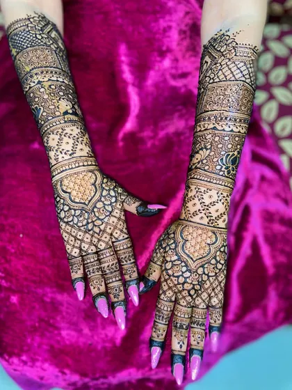 A gorgeous full-hand mehandi design with a mix of grids, florals, and paisley patterns, creating a rich and dense look that extends up the arms.