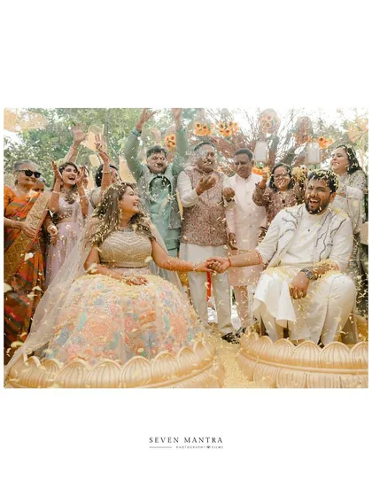 A moment of celebration with family and friends. The couple is showered with flower petals, their joyous expressions at the center of this happy memory. The bride's pastel lehenga offers a soft contrast to the traditional yellow theme.