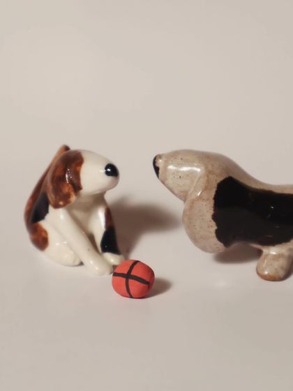 Two miniature dog figurines, a beagle and a basset hound, playing with a small red ball. These tiny sculptures capture the playful spirit of our furry friends.