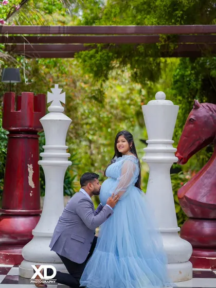 A playful and romantic pose on the giant chessboard, with the partner kneeling to kiss the baby bump.