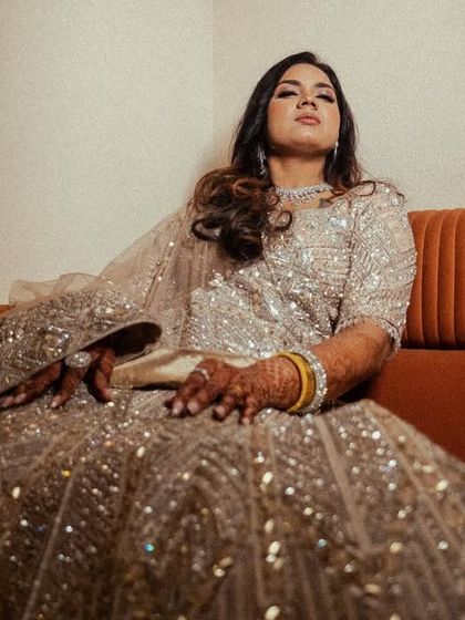 A portrait of the bride sitting on a couch, her sequined lehenga catching the light beautifully.