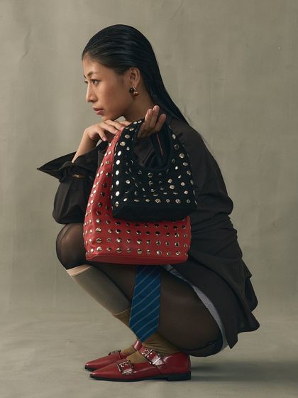 Sharp lines and studded details create a sense of quiet power. Here, the Icon studded bag is shown in multiple sizes and colors, alongside a pair of red patent buckled flats, showcasing the versatility of the collection.