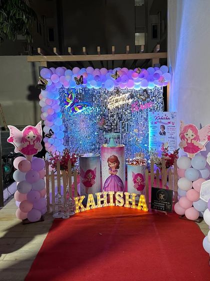 A fairy and butterfly-themed entrance with a red carpet. The setup includes a shimmer wall, character cutouts, and personalized photo boards to welcome guests.