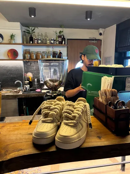 The coffee-themed custom sneakers sitting on a cafe counter, with a barista in the background.
