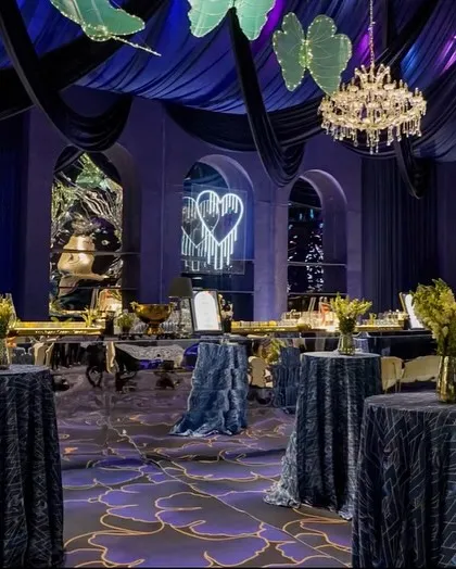 The bar area for the blue cocktail event, set against a backdrop of elegant arches and a neon sign of two swans. The mirrored bar front reflects the deep colors and lights of the room.