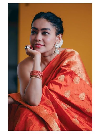 A vibrant portrait of a model in a bright orange saree. Her happy expression and the rich colors create a joyful and lively image.