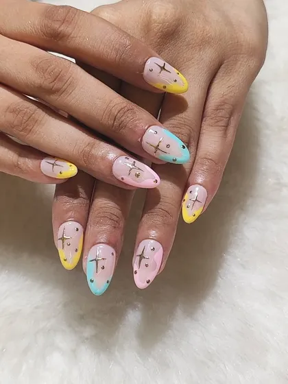 A playful take on celestial nails. This design features a sheer base with pastel color-blocked tips in yellow, pink, and blue, all decorated with golden star charms and dots.