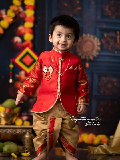 A handsome little boy in a festive red and gold outfit, smiling brightly during his traditional-themed photoshoot.
