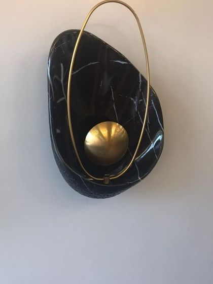 A detailed view of the 'Bird Nest' wall lamp. This piece showcases the beautiful contrast between the organic, polished black marble and the delicate, ring-shaped brass element that encircles the light source.