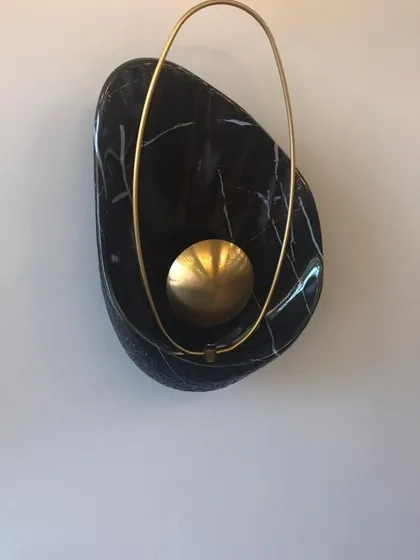 A detailed view of the 'Bird Nest' wall lamp. This piece showcases the beautiful contrast between the organic, polished black marble and the delicate, ring-shaped brass element that encircles the light source.