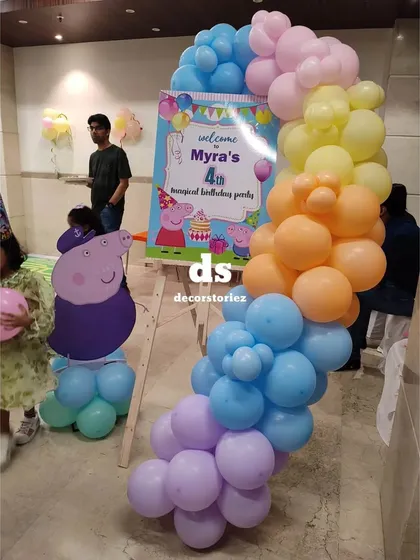 A custom welcome sign on an easel for a Peppa Pig party, decorated with a matching pastel balloon garland to greet guests as they arrive.