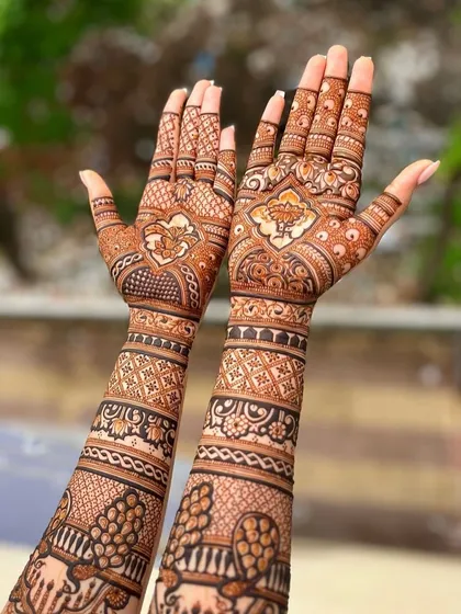 This design shows how beautifully a full bridal mehndi can be displayed. The pattern covers the arms with traditional bands, paisleys, and floral elements, held up against a natural background.
