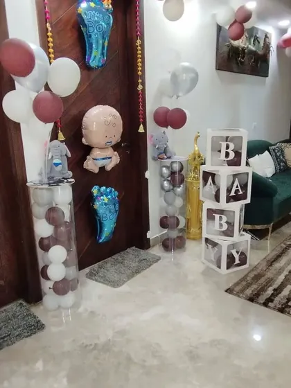 A charming setup to welcome a baby boy home. This decoration includes transparent "BABY" boxes filled with balloons, balloon pillars, and cute baby-themed foil balloons.