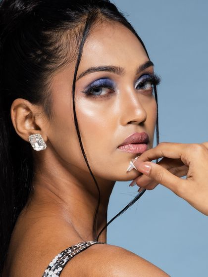 A close-up beauty portrait with a focus on the model's intense gaze and flawless makeup. The stray strands of hair add a touch of softness to the look.