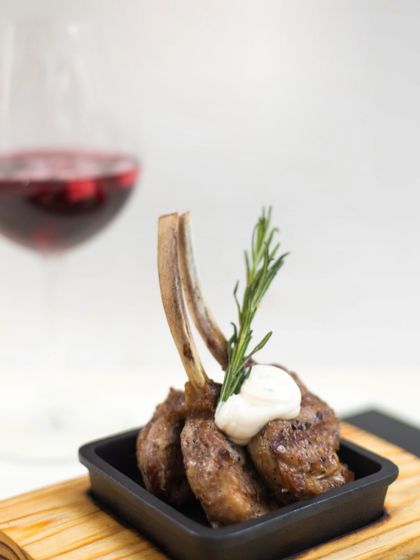 A single, perfectly cooked lamb chop served as a tapa, garnished with rosemary and a dollop of creamy sauce.