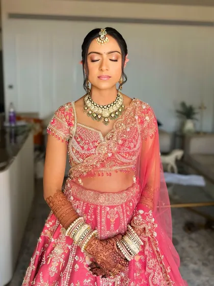 A moment of calm before the ceremony. The soft updo with floral accents complements the delicate embroidery on her pink lehenga.