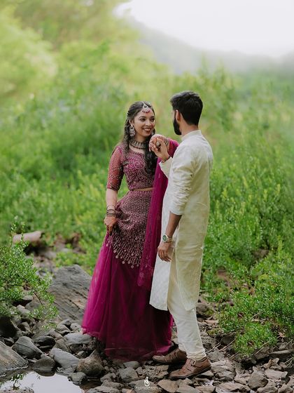 A romantic moment in a lush green clearing. The rich colors of her lehenga stand out beautifully against the vibrant natural background.