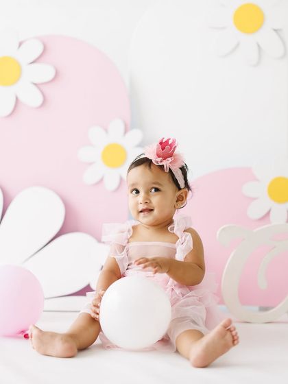 All smiles amidst the celebration. This little girl, surrounded by balloons and her birthday setup, looks so happy and content during her first birthday party photoshoot.