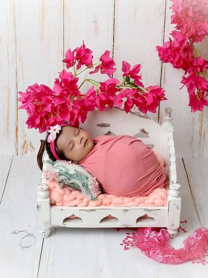 Pretty in pink. This baby girl sleeps on a tiny white bed, framed by vibrant pink bougainvillea, creating a beautiful and feminine floral portrait.