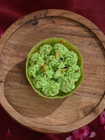 My light and nutty pistachio ghewar, presented on a wooden platter, is a perfect blend of traditional flavour and gourmet quality.