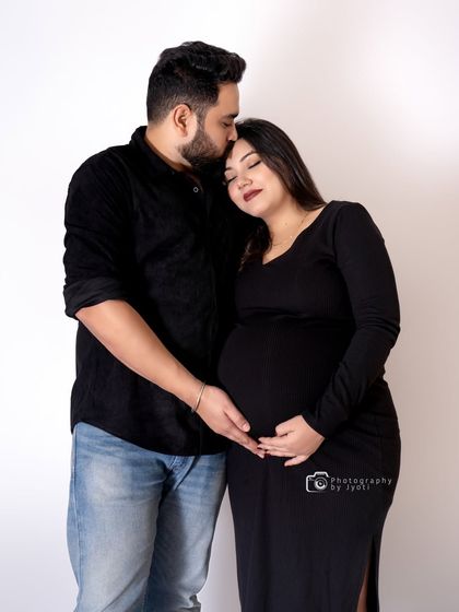 A tender moment between a couple, dressed in black for a minimalist and modern maternity portrait. The focus is purely on their affection and anticipation.