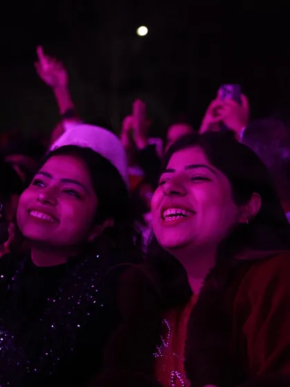 Two friends smiling and looking up at the stage, bathed in pink light. We create a safe and vibrant atmosphere for everyone.